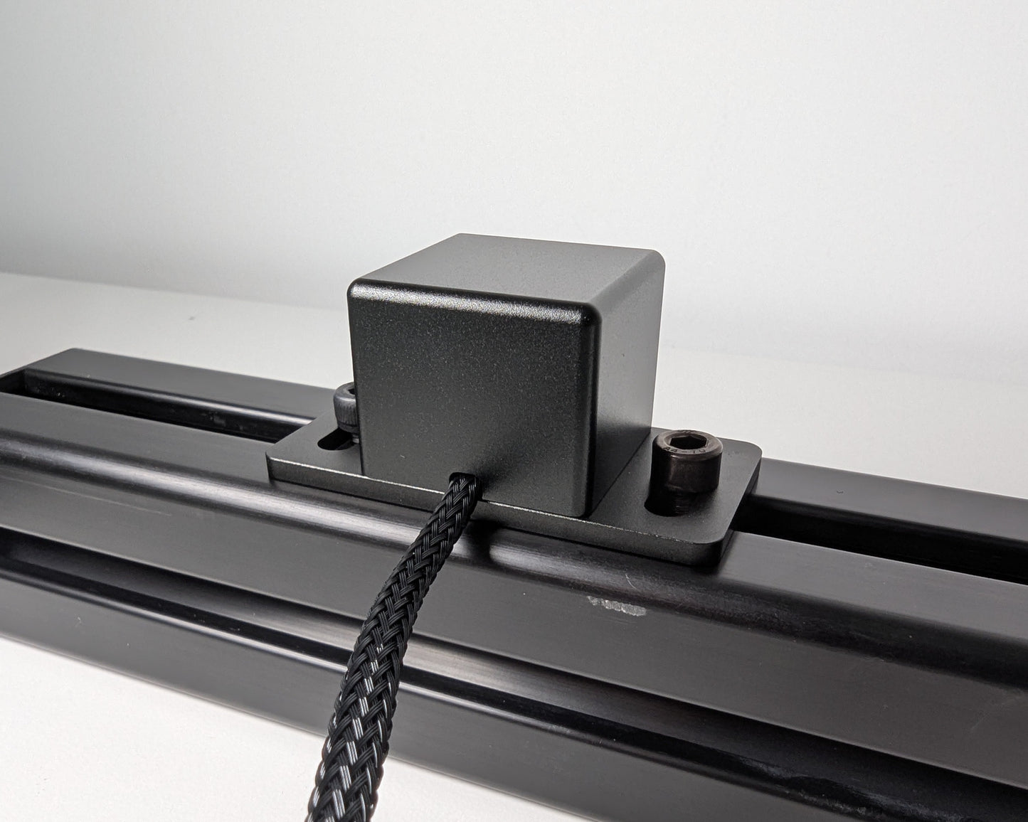 Close-up of the rear of JC Power Button mounted to black 4040 profile. The power button is a black box attached to the profile with 2 bolts. The rear view also shows the black braided cable.