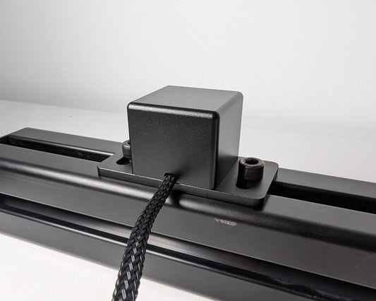 Close-up of the rear of JC Power Button mounted to black 4040 profile. The power button is a black box attached to the profile with 2 bolts. The rear view also shows the black braided cable.