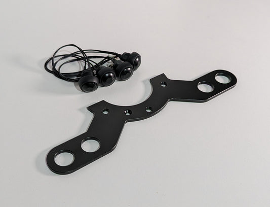 The JCSS 4 Button bracket on a white surface with four buttons and cables. The bracket is black aluminium finish with a half circular feature on the centre with two long arms with two holes at each end for mounting buttons.
