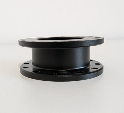The side view of the JC 30mm Spacer.  A black aluminium cylindrical object with a flange top and bottom. Bolt holes for mounting are shown around the visible diameter.  Object is placed on a white surface with a white background.