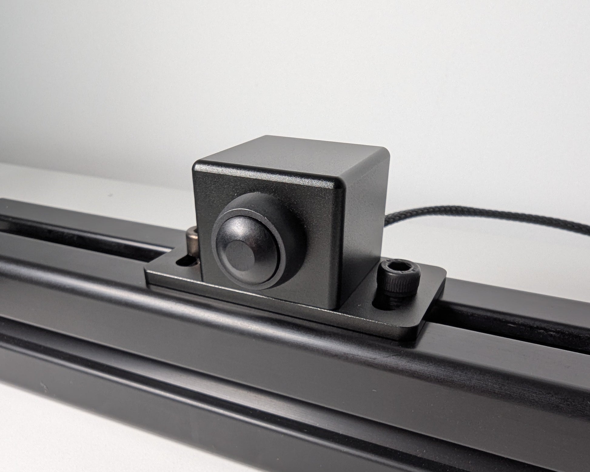 Close-up of the JC Power Button mounted to black 4040 profile.  The power button is a black box with a black button attached with 2 bolts.