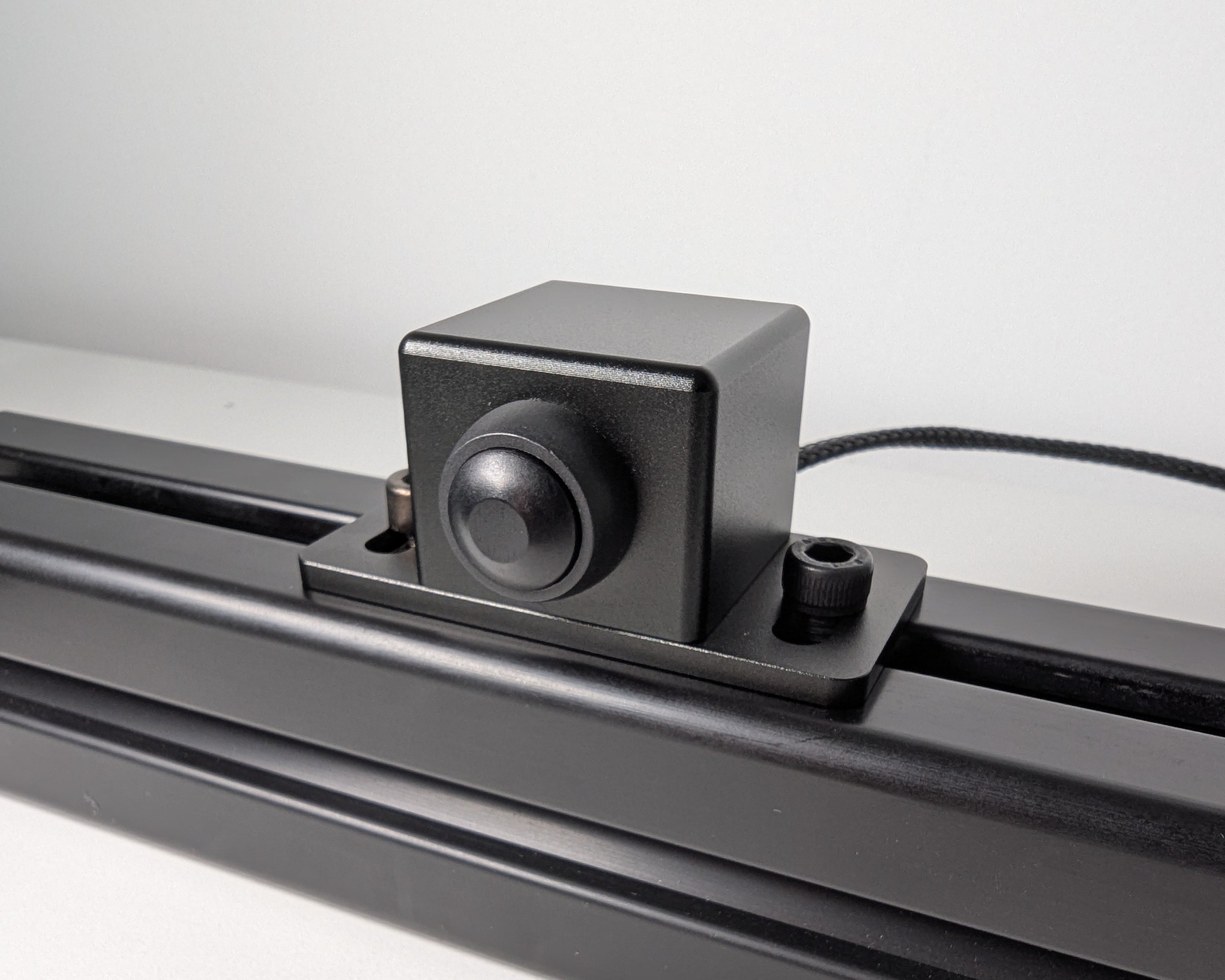 Close-up of the JC Power Button mounted to black 4040 profile.  The power button is a black box with a black button attached with 2 bolts.