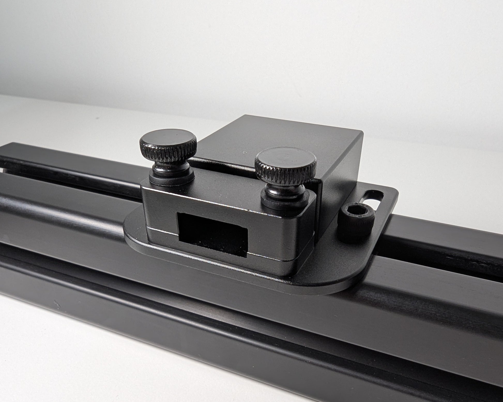 Close-up of the JC USB Power Injector mounted to black 4040 profile.  The USB power injector is a black box attached to the profile with 2 bolts.  The front view shows the two black thumbscrews and hold down for securely mounting a cable.