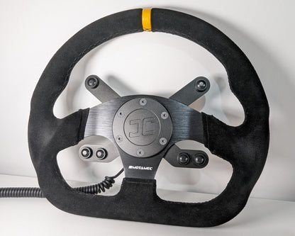 Black steering wheel with 'JC' branding on a white background  The wheel has a JC wheel hub with a top 2 button bracket and a bottom 4 button bracket with black buttons mounted.  The hub has a black coiled cable.